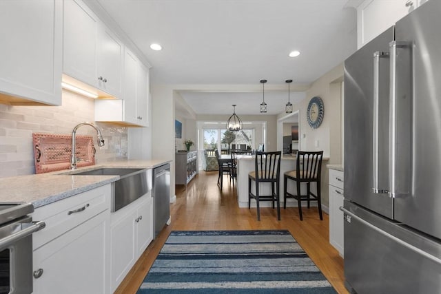 kitchen with a sink, appliances with stainless steel finishes, white cabinetry, light wood-type flooring, and backsplash