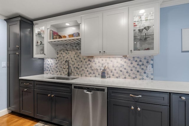 kitchen featuring stainless steel dishwasher, a sink, light wood-type flooring, decorative backsplash, and glass insert cabinets
