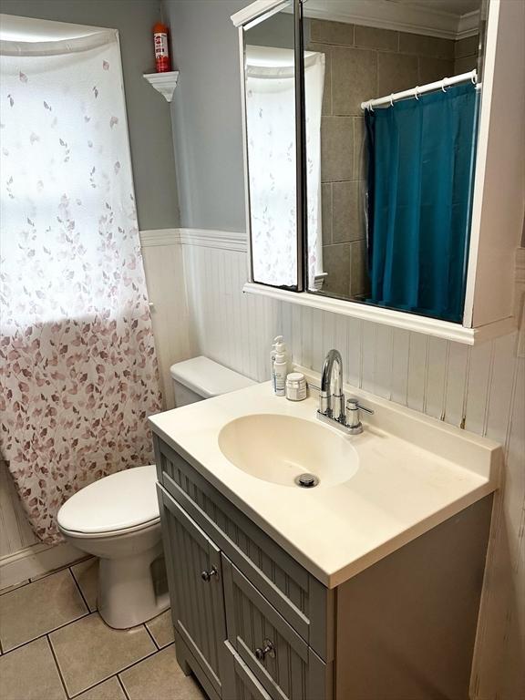 full bath with tile patterned flooring, curtained shower, toilet, wainscoting, and vanity