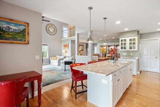 kitchen with sink, white cabinetry, hanging light fixtures, light stone counters, and an island with sink