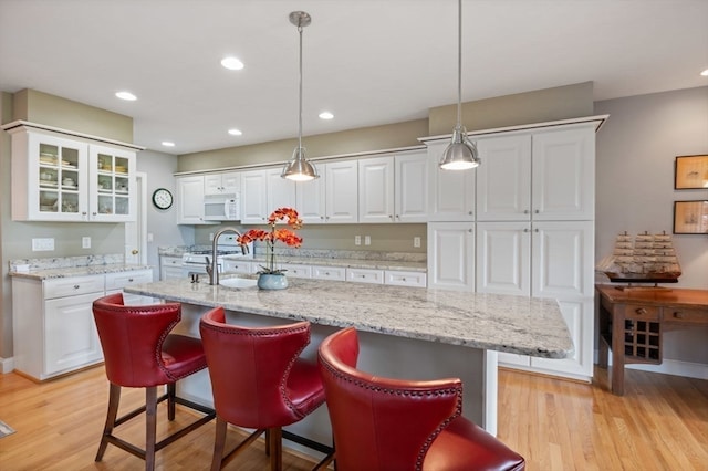 kitchen featuring white appliances, white cabinets, light hardwood / wood-style floors, hanging light fixtures, and a center island with sink