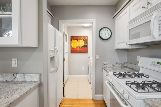 kitchen with light stone counters, light hardwood / wood-style flooring, white appliances, washing machine and dryer, and white cabinets
