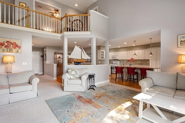living room featuring sink, light carpet, ceiling fan, and a towering ceiling