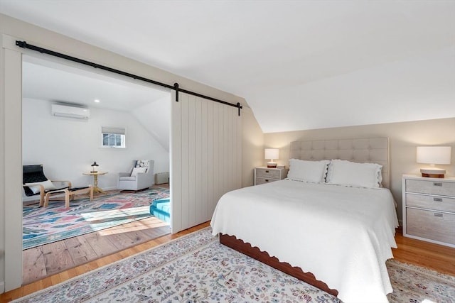 bedroom with a barn door, wood finished floors, a wall mounted AC, and lofted ceiling