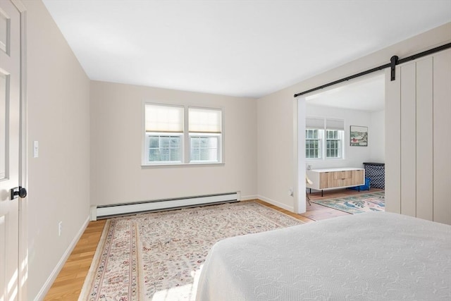 bedroom featuring a baseboard heating unit, wood finished floors, baseboards, and a barn door