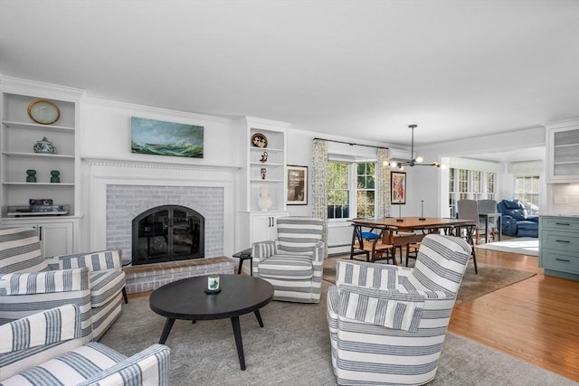 living area with light wood-type flooring, built in features, a brick fireplace, a chandelier, and a baseboard radiator