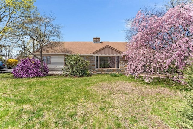 rear view of property with a lawn, a chimney, and stone siding