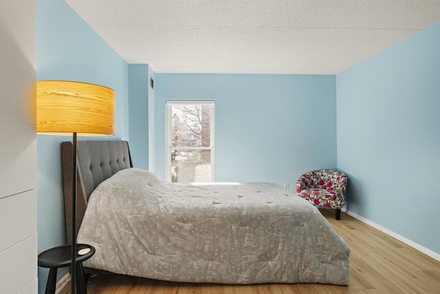 bedroom with a textured ceiling, baseboards, and wood finished floors