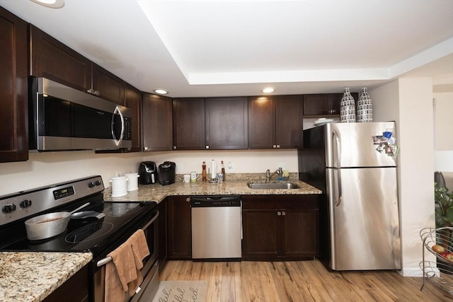 kitchen featuring light stone countertops, light wood-style flooring, a sink, stainless steel appliances, and dark brown cabinetry