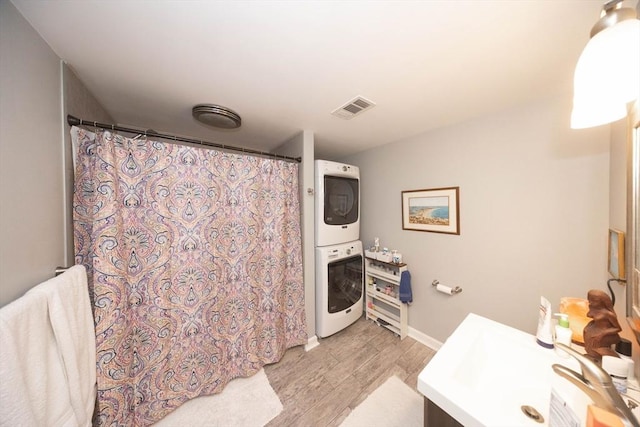 bathroom featuring visible vents, wood finished floors, a shower with shower curtain, stacked washer / drying machine, and vanity