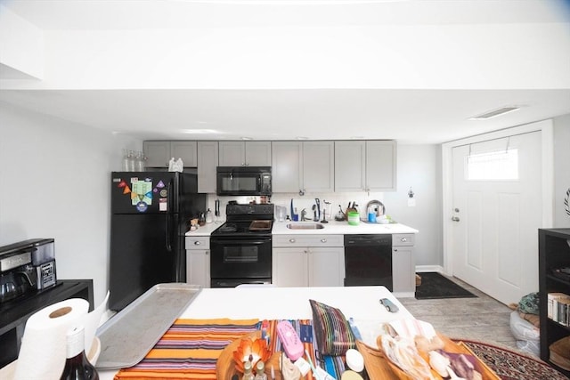 kitchen featuring gray cabinetry, light countertops, wood finished floors, black appliances, and a sink