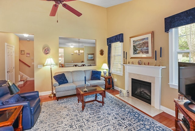 living room featuring ceiling fan with notable chandelier, crown molding, hardwood / wood-style floors, and a tile fireplace