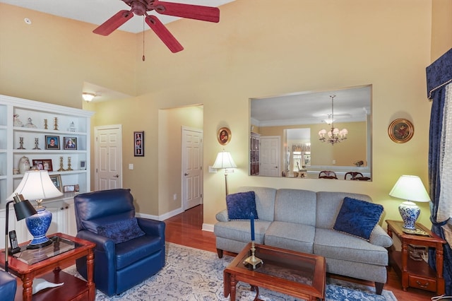 living room with wood-type flooring, ceiling fan with notable chandelier, crown molding, and a towering ceiling