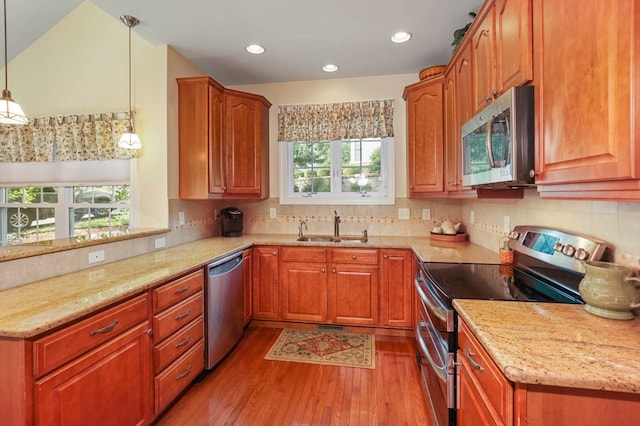 kitchen with hanging light fixtures, sink, light hardwood / wood-style flooring, appliances with stainless steel finishes, and light stone countertops