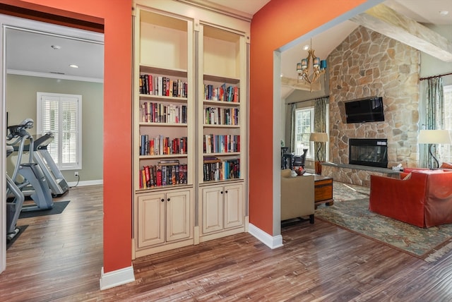 living room featuring vaulted ceiling, a stone fireplace, wood-type flooring, ornamental molding, and a chandelier