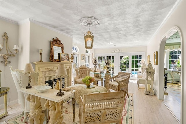 sitting room featuring arched walkways, a fireplace, crown molding, light wood-style flooring, and french doors