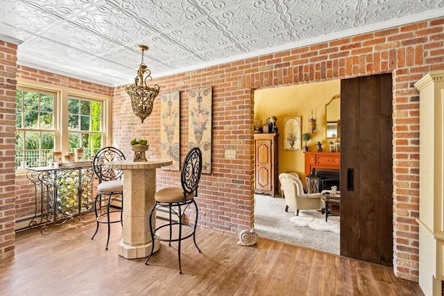 dining area featuring wood finished floors, an ornate ceiling, brick wall, a fireplace, and ornamental molding