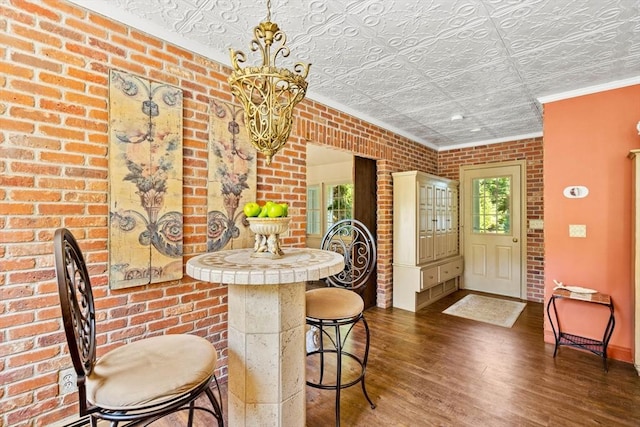 dining space featuring wood finished floors, an ornate ceiling, brick wall, a chandelier, and ornamental molding