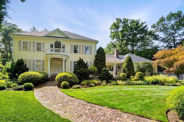 colonial house featuring a front yard, a chimney, and a balcony