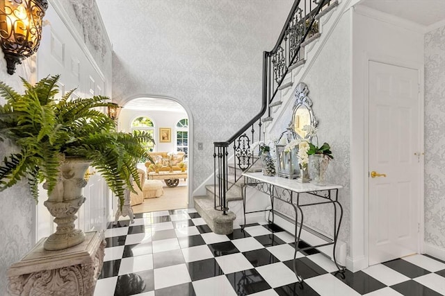 foyer entrance featuring stairway, arched walkways, tile patterned floors, a chandelier, and ornamental molding