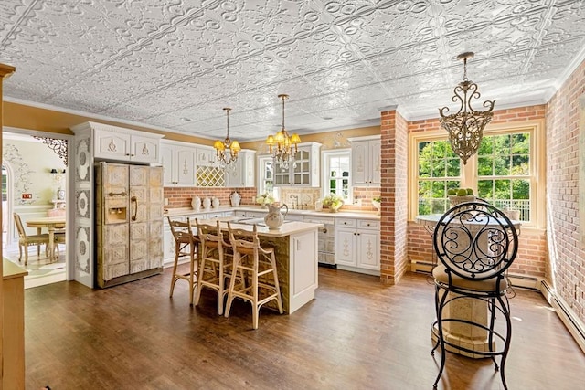 kitchen with a chandelier, refrigerator with ice dispenser, light countertops, a kitchen bar, and dark wood-type flooring