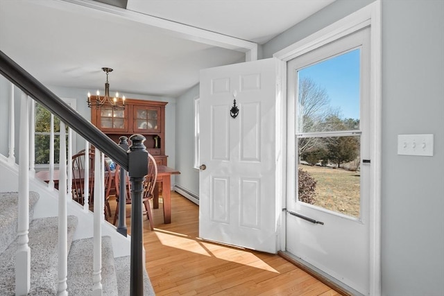 foyer entrance featuring a chandelier, baseboard heating, a healthy amount of sunlight, and light wood-style flooring