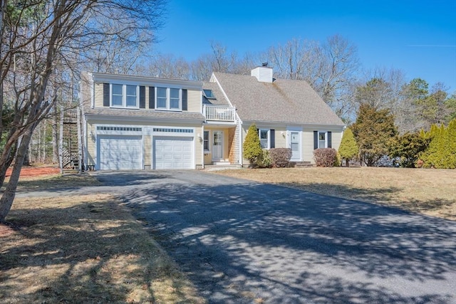 view of front facade featuring a shingled roof, aphalt driveway, a chimney, a balcony, and an attached garage