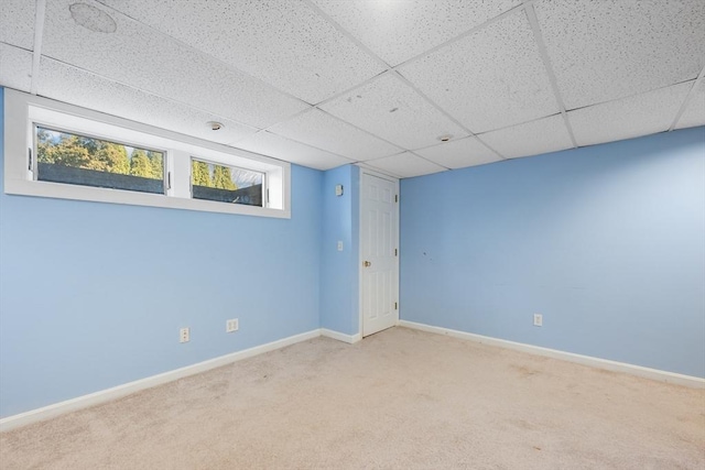 carpeted empty room featuring a drop ceiling and baseboards