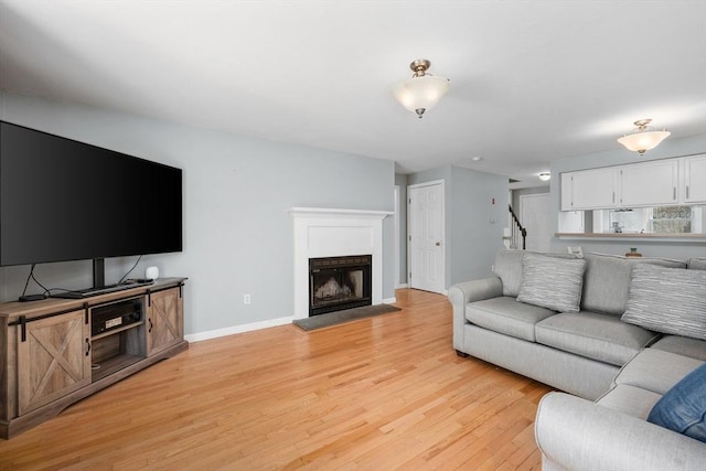 living room with baseboards, a fireplace with raised hearth, light wood-style flooring, and stairs