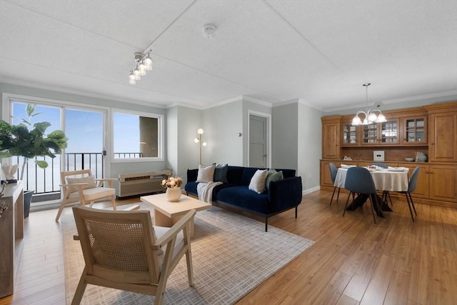 living area with crown molding, light wood-type flooring, baseboards, and a notable chandelier