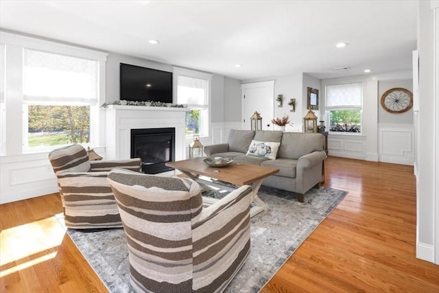 living area with a decorative wall, a glass covered fireplace, and light wood-style floors