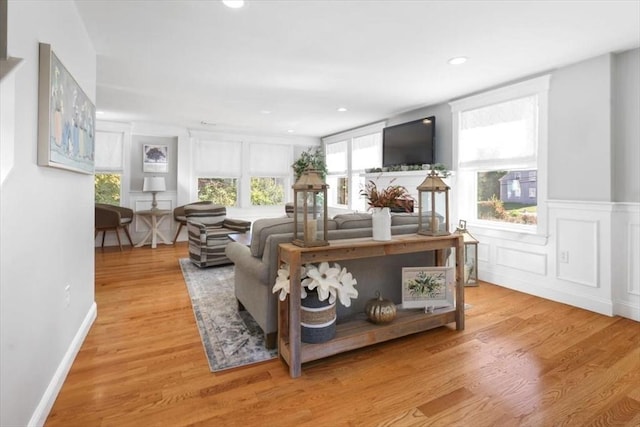 living room featuring wainscoting, light wood-style flooring, a decorative wall, and recessed lighting