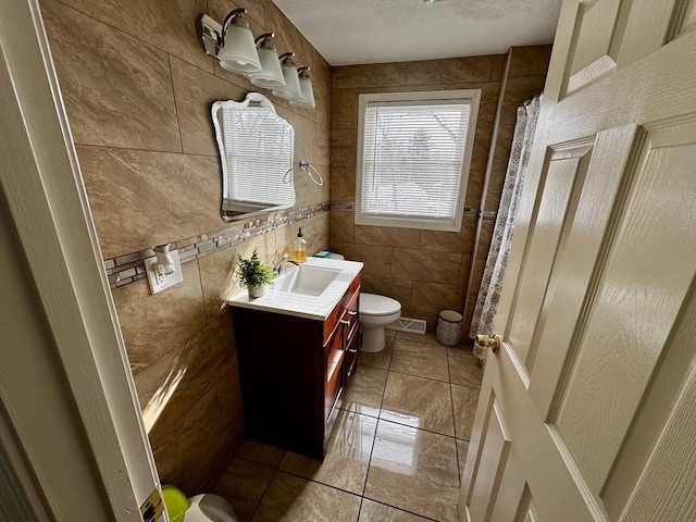 bathroom featuring tile patterned floors, toilet, tile walls, a textured ceiling, and vanity