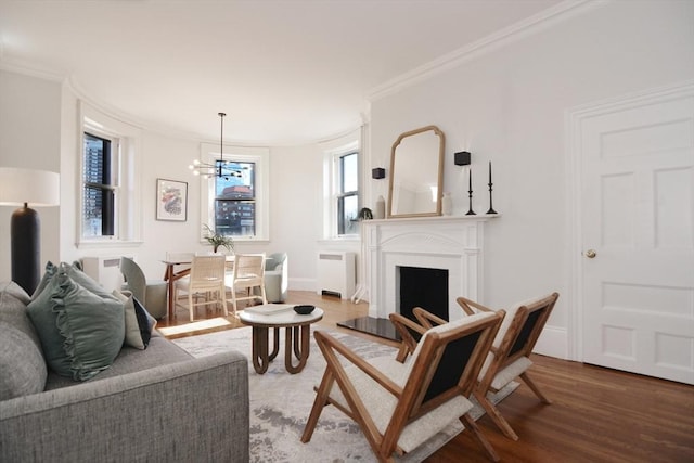 living room with radiator, wood finished floors, a fireplace with raised hearth, ornamental molding, and a chandelier