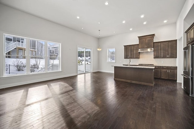 kitchen with sink, high quality fridge, dark hardwood / wood-style flooring, a kitchen island with sink, and backsplash