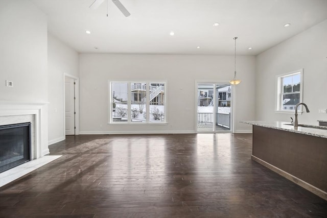 unfurnished living room featuring dark hardwood / wood-style flooring, sink, ceiling fan, and a fireplace