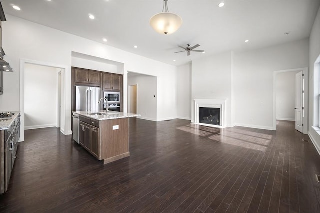 kitchen featuring an island with sink, appliances with stainless steel finishes, light stone counters, and dark brown cabinetry