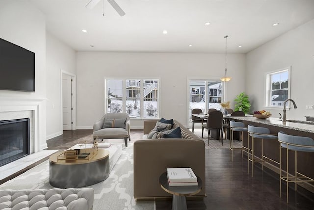 living room with a premium fireplace, sink, dark wood-type flooring, and ceiling fan