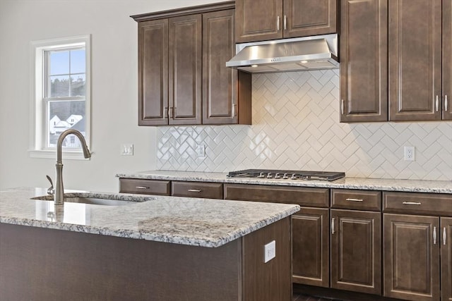 kitchen featuring ventilation hood, tasteful backsplash, sink, light stone counters, and dark brown cabinetry