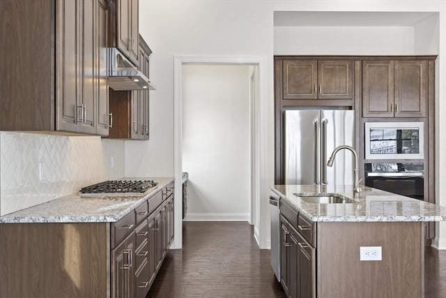 kitchen with a kitchen island with sink, light stone countertops, dark brown cabinets, and stainless steel appliances