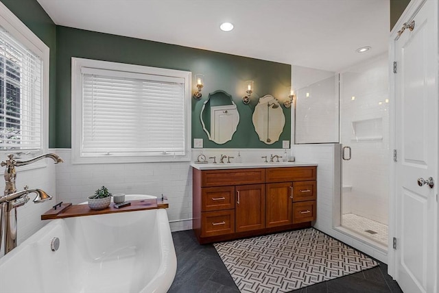 bathroom with a sink, tile walls, a freestanding bath, double vanity, and a stall shower