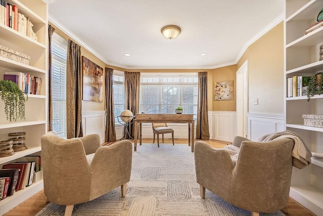 living area with a wainscoted wall, ornamental molding, wood finished floors, and a decorative wall