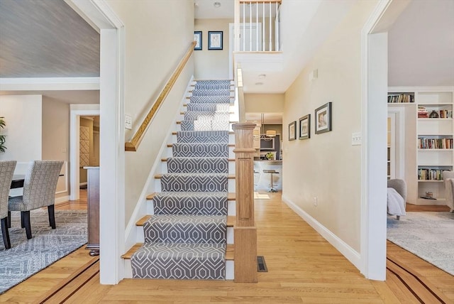 stairway with a high ceiling, wood finished floors, and baseboards