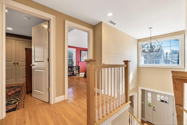 corridor featuring visible vents, baseboards, an upstairs landing, and light wood-style floors