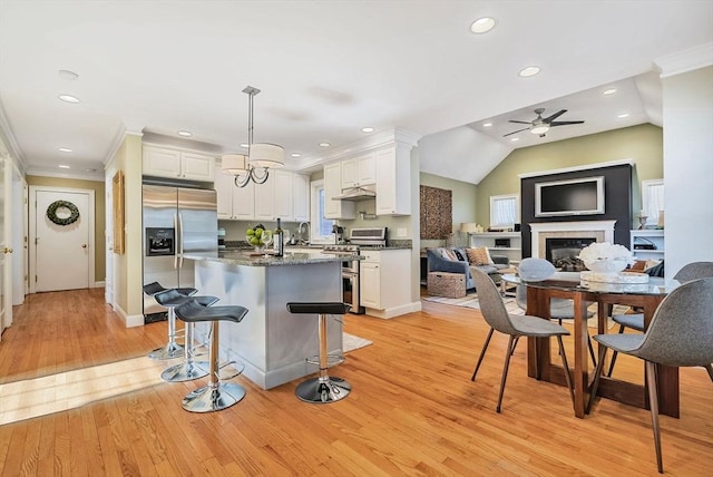 kitchen with crown molding, appliances with stainless steel finishes, a glass covered fireplace, open floor plan, and white cabinets