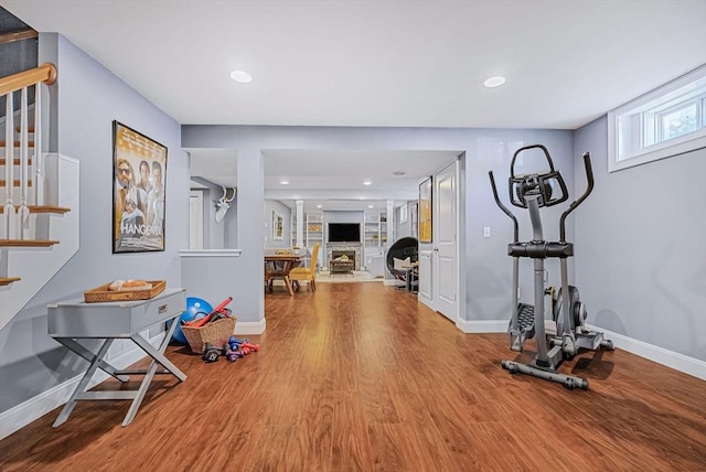 exercise room with a fireplace with raised hearth, recessed lighting, wood finished floors, and baseboards