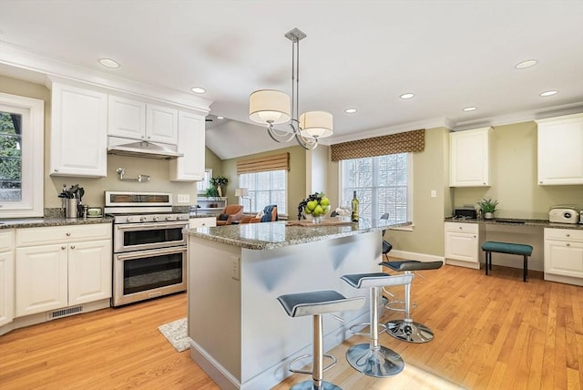 kitchen featuring visible vents, white cabinets, double oven range, under cabinet range hood, and a kitchen breakfast bar