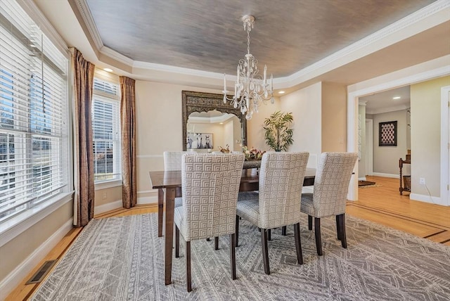 dining area featuring wood finished floors, a raised ceiling, visible vents, and crown molding