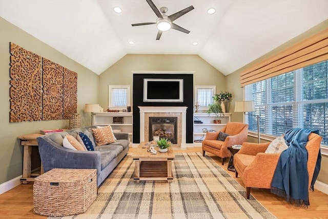 living area featuring baseboards, a ceiling fan, lofted ceiling, a premium fireplace, and wood finished floors