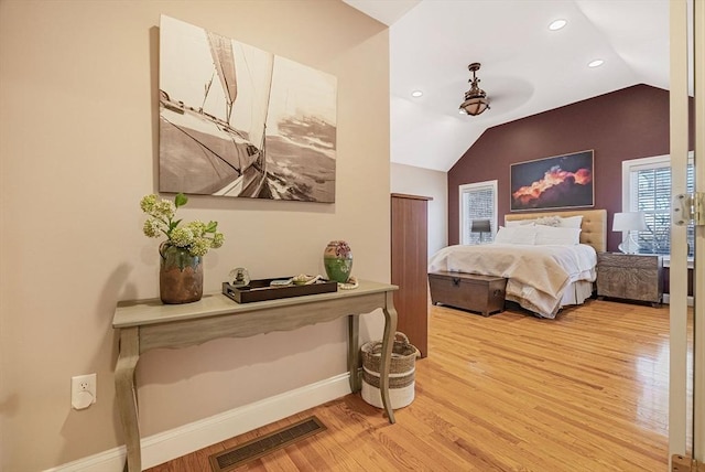 bedroom with baseboards, visible vents, vaulted ceiling, and light wood finished floors